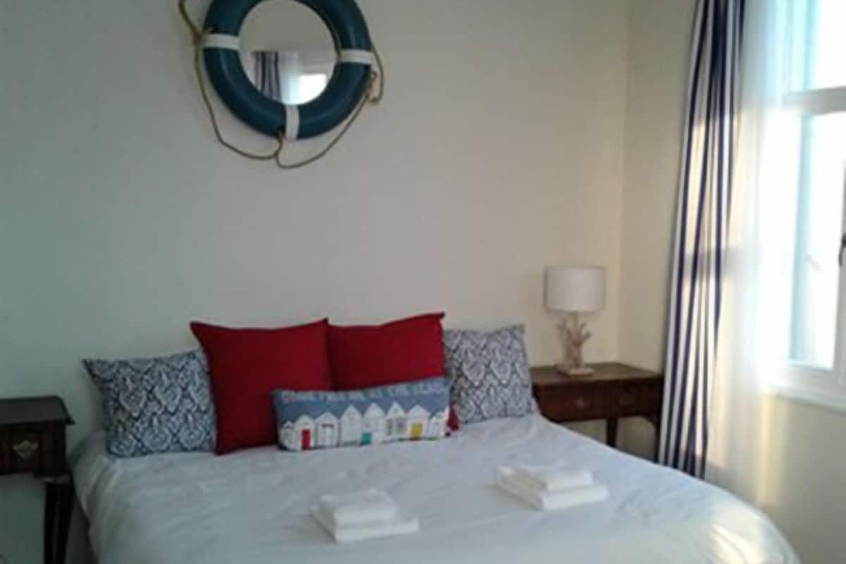 A bedroom with a bed, pillows, a bedside table, a lamp, and a window with curtains.