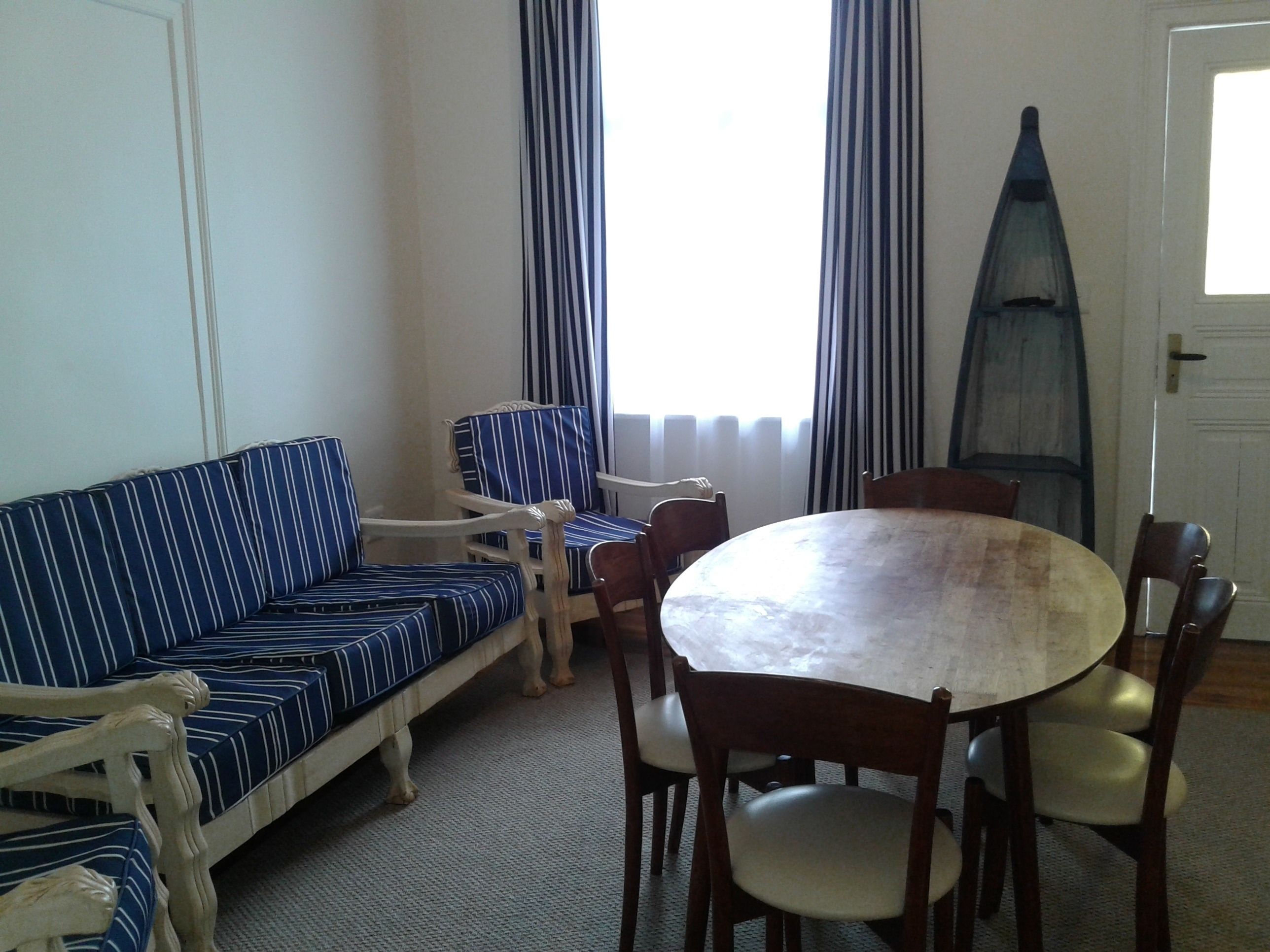Ein Zimmer mit einem gestreiften Sofa, einem runden Tisch mit Stühlen und einem Fenster mit Vorhängen.
