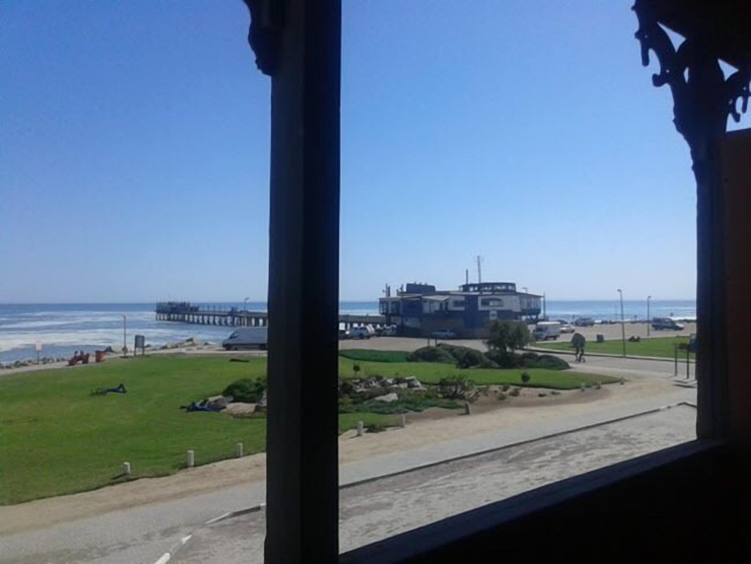 A view of a beach with a pier, a grassy area, and a building in the background.