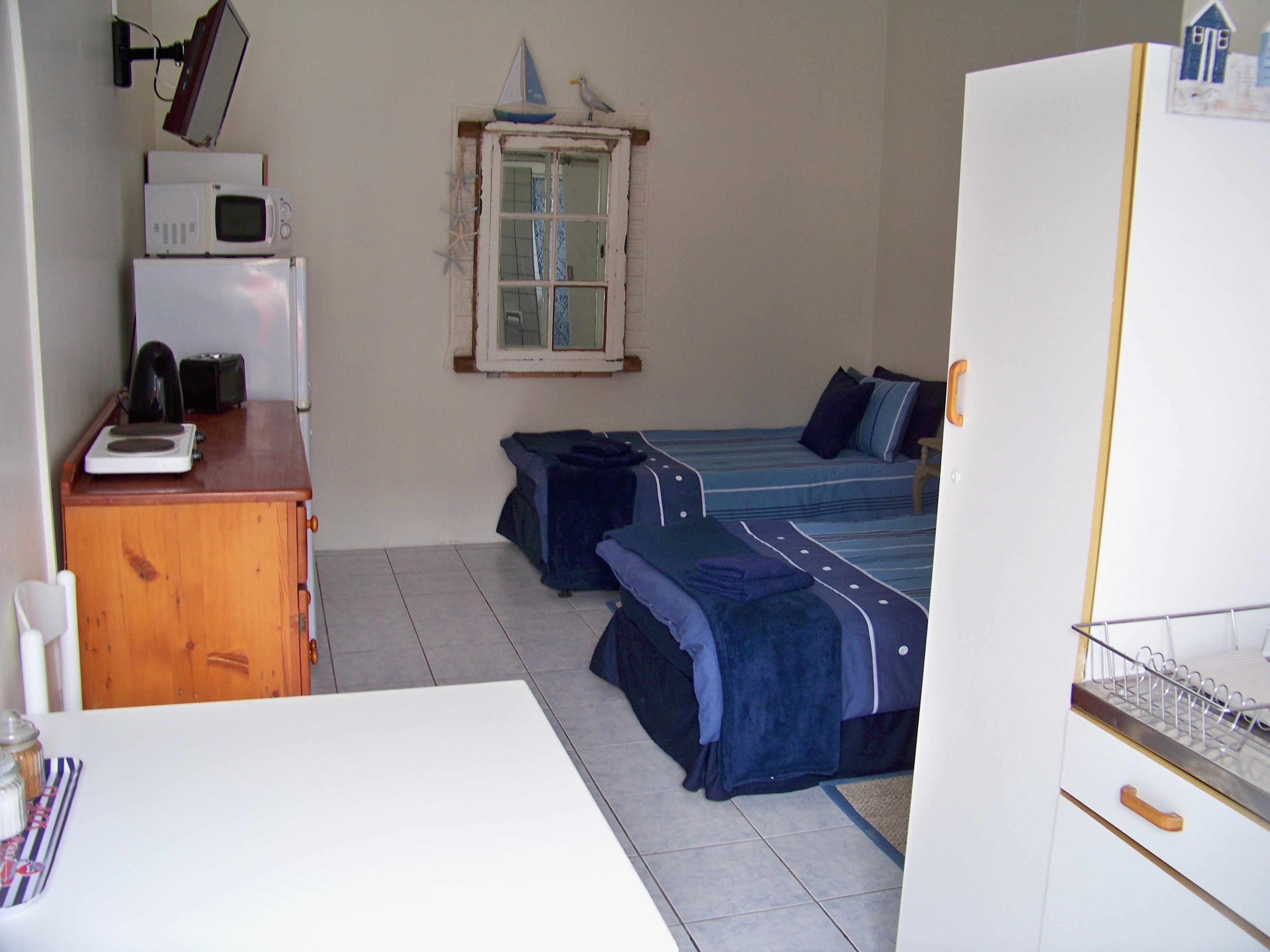 A small, compact room with a kitchenette area, two beds, and a window with a view.