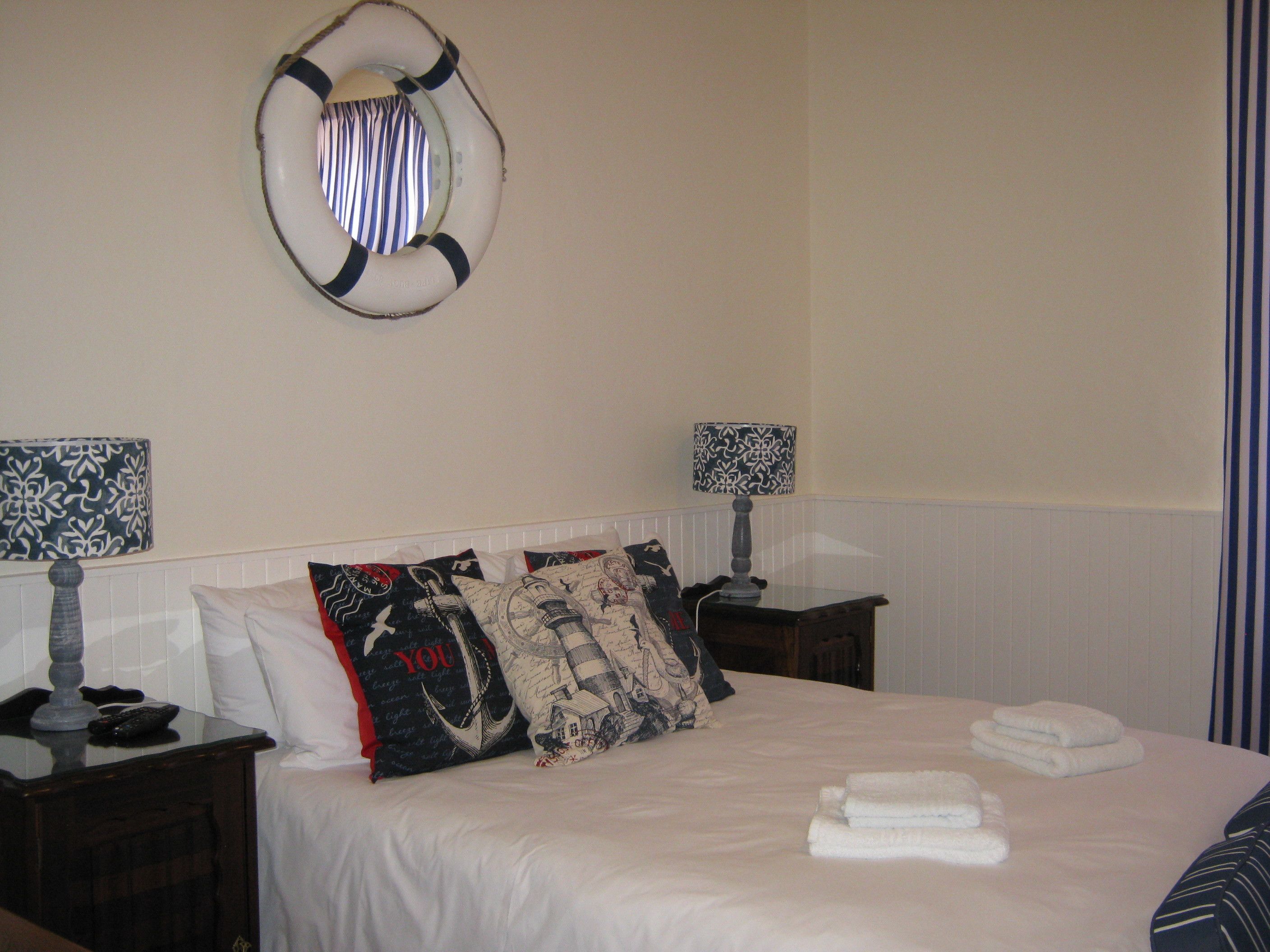 A neatly made bed with white linens and several decorative pillows, a bedside lamp, and a wall-mounted life preserver.