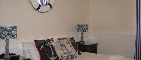A neatly made bed with white linens and several decorative pillows, a bedside lamp, and a wall-mounted life preserver.