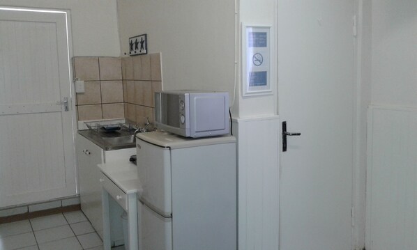 A compact kitchen with a microwave on top of a refrigerator, a sink, and a small countertop.