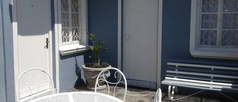 Un patio con una mesa y sillas de metal blanco, una planta en maceta y un banco blanco.