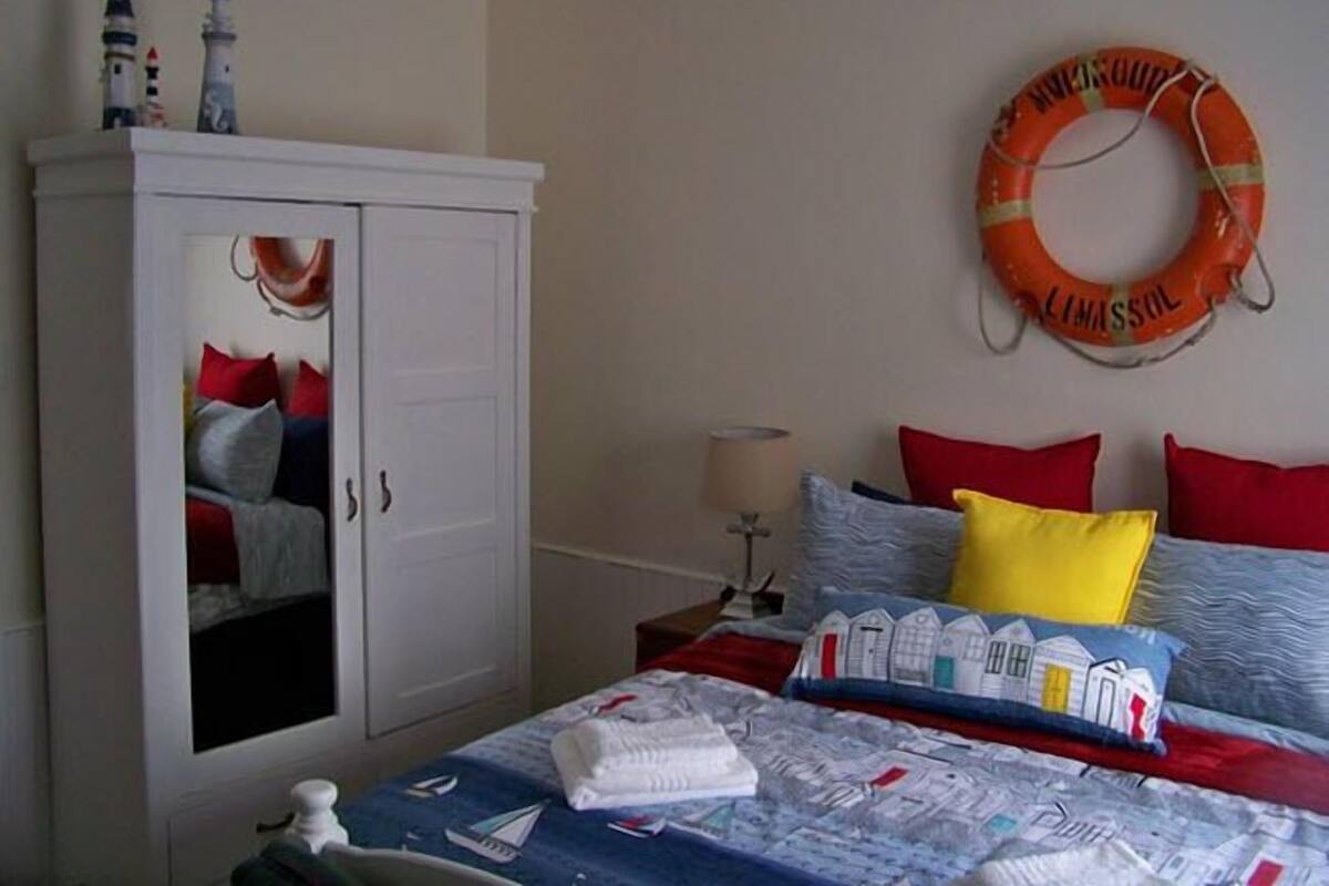 A bedroom with a bed, a wardrobe, a nightstand, a lamp, and a life ring on the wall.