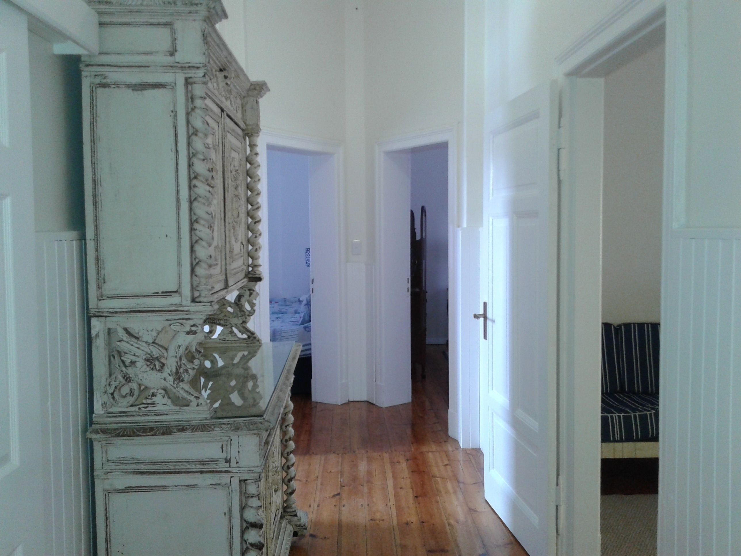 Um corredor com piso de madeira, paredes brancas e um armário branco grande, ornamentado e desgastado à esquerda.