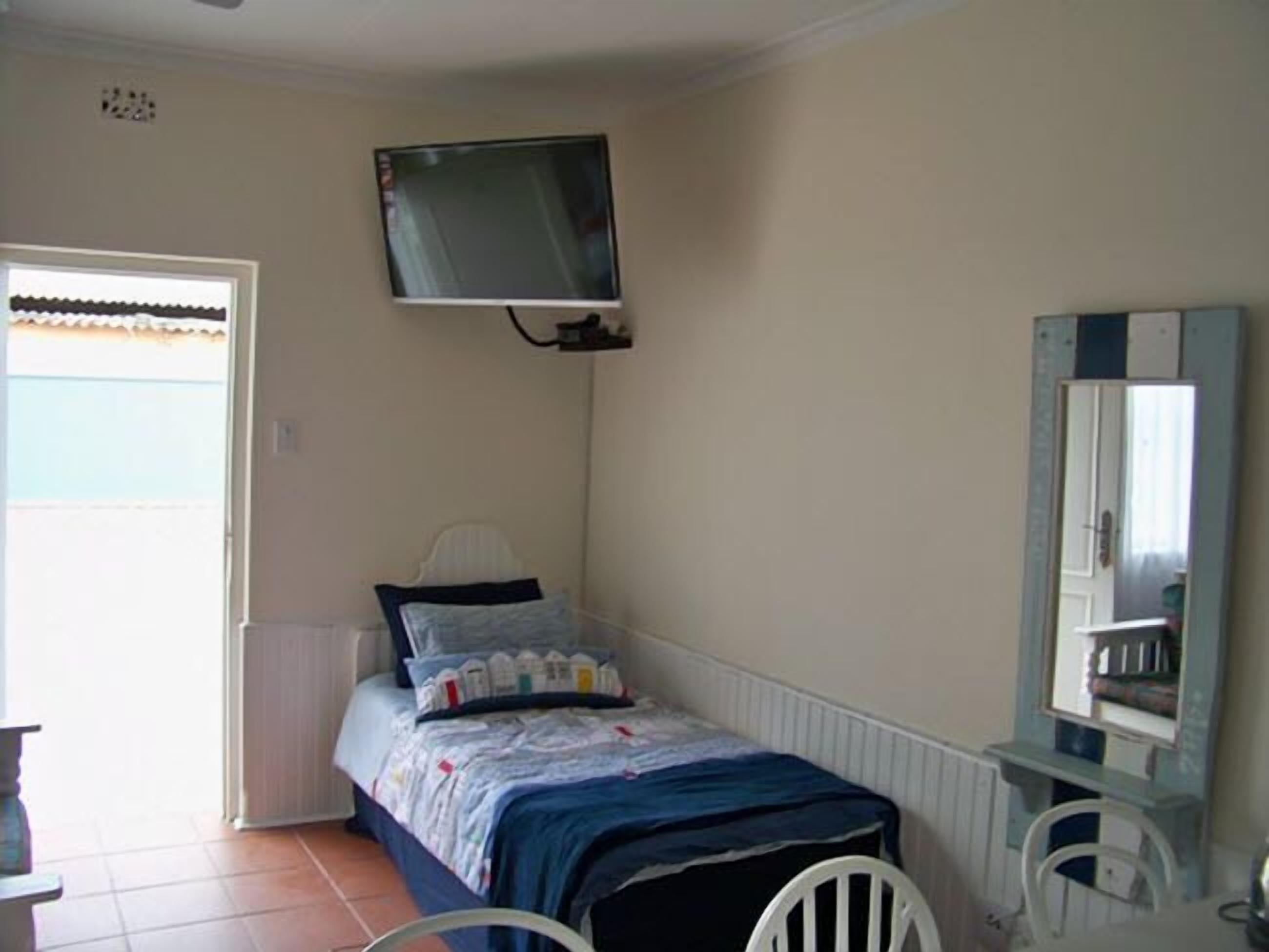 Un dormitorio pequeño con una cama, televisor montado en la pared, una silla y un tocador con espejo.
