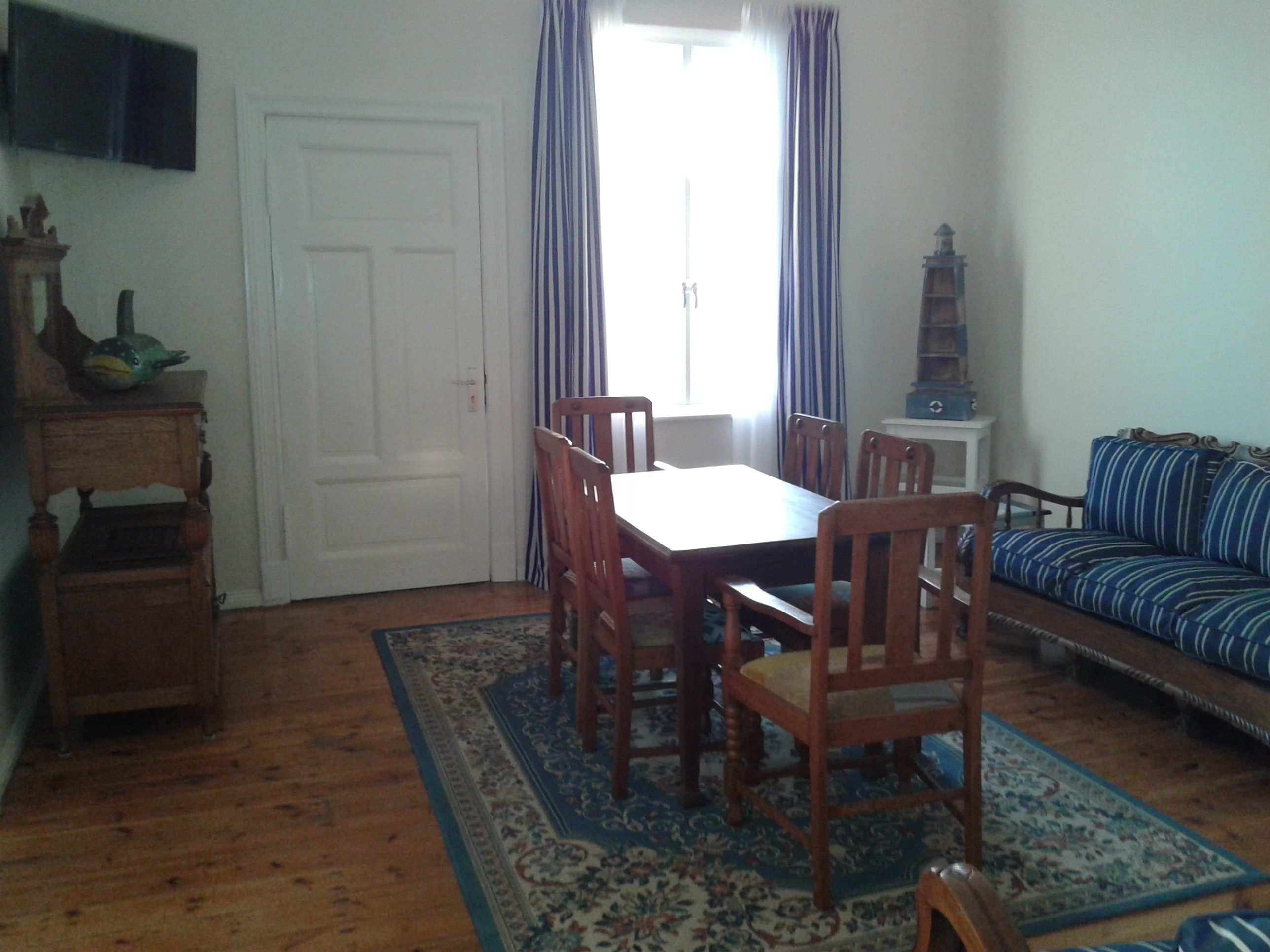 A room with a dining table, chairs, a sofa, a television, and a window with curtains.