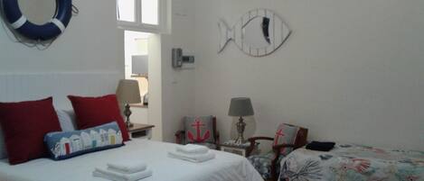 A bedroom with a bed, two bedside tables, a nightstand, a fish-shaped wall decoration, a life ring, and a window.