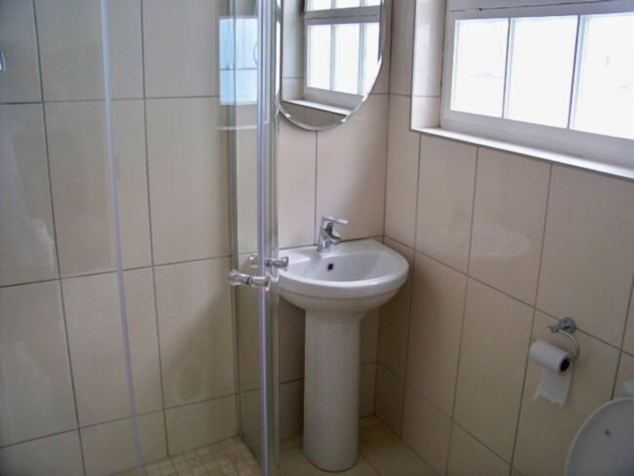 A bathroom with a glass shower enclosure, a pedestal sink, and a toilet.