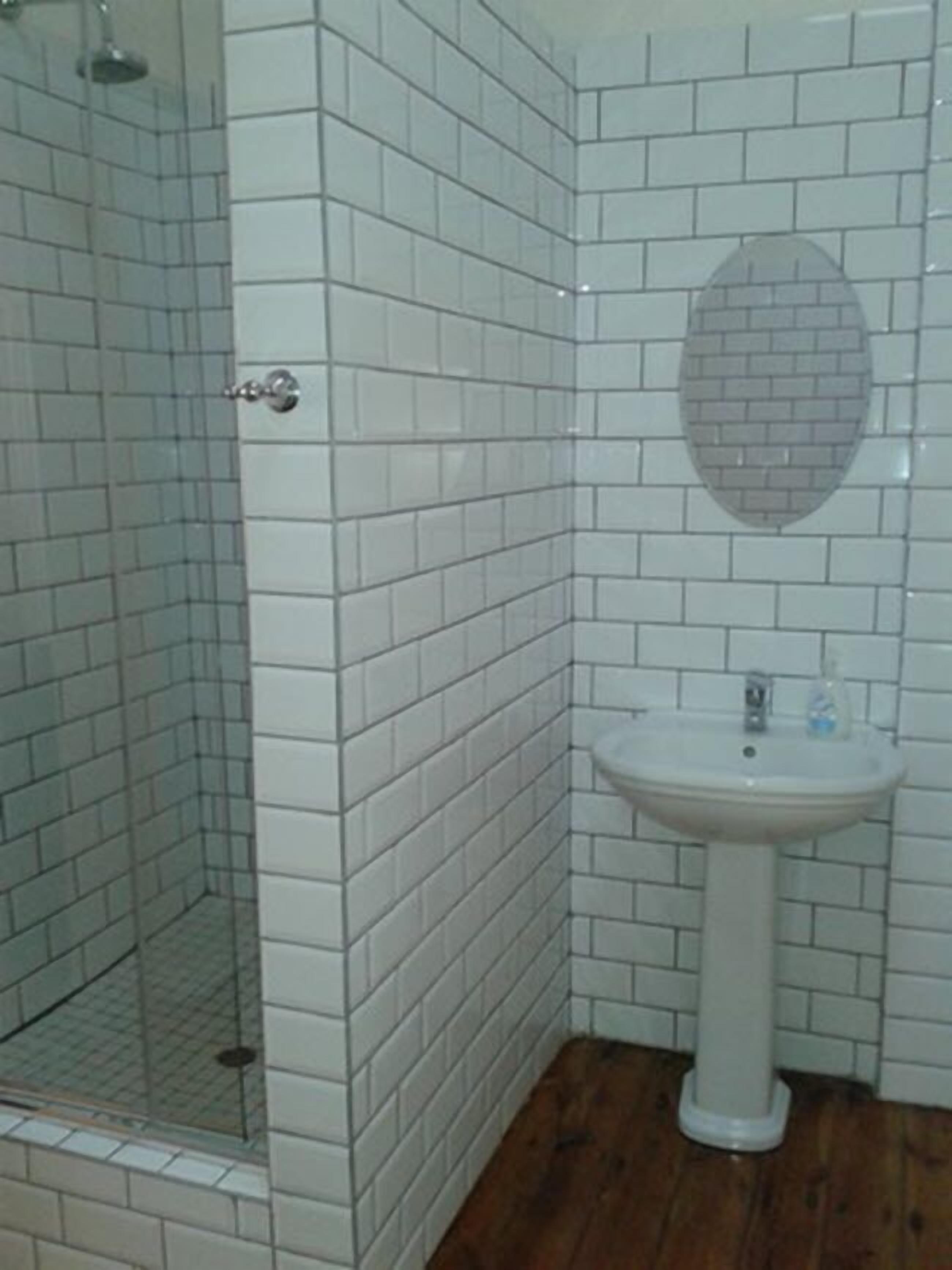 A bathroom with white tiled walls, a wooden floor, a sink, and a glass shower enclosure.