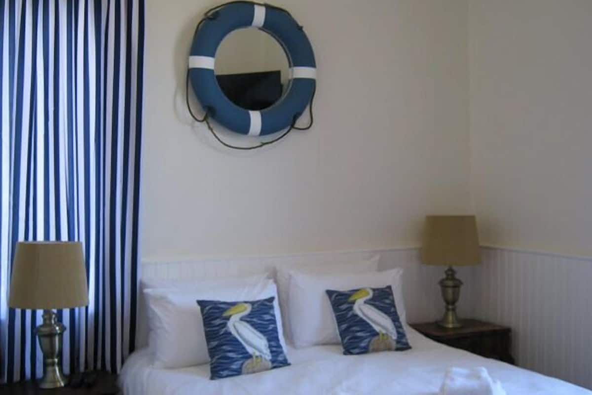 A hotel room with a bed, two pillows with a bird design, a life ring on the wall, and striped curtains.