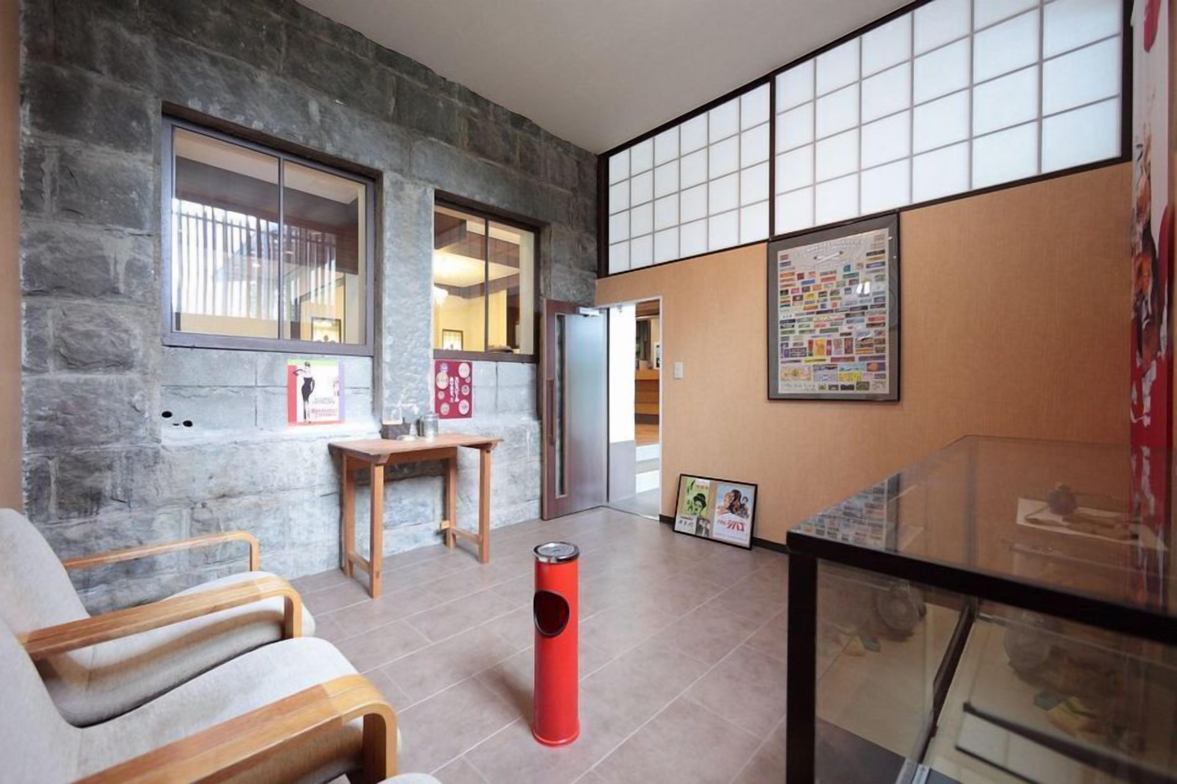 A modern interior with a stone wall, a wooden chair, a small table, a red trash bin, and a glass display case.