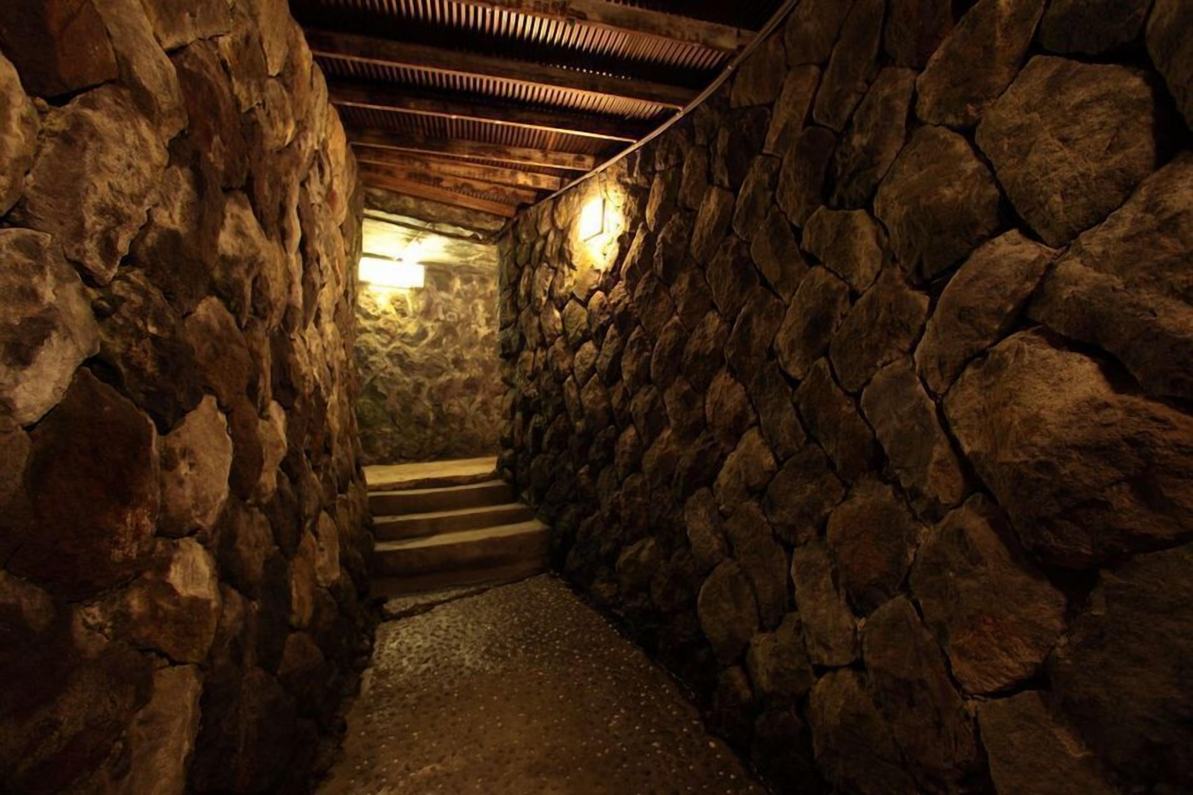 Un couloir aux murs de pierre, avec un escalier en bois menant à un niveau supérieur.