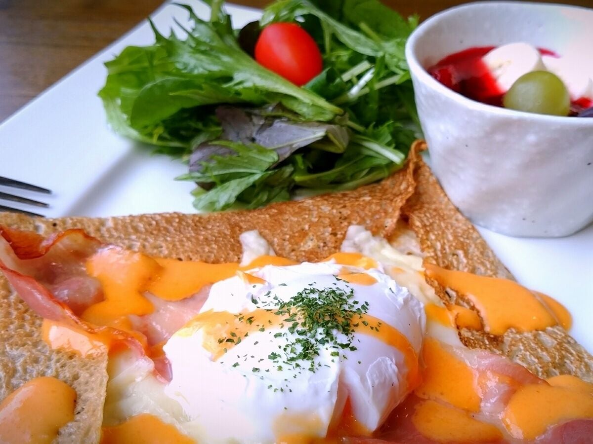 A breakfast plate with toast, poached eggs, and bacon, accompanied by a side salad and a cup of fruit.