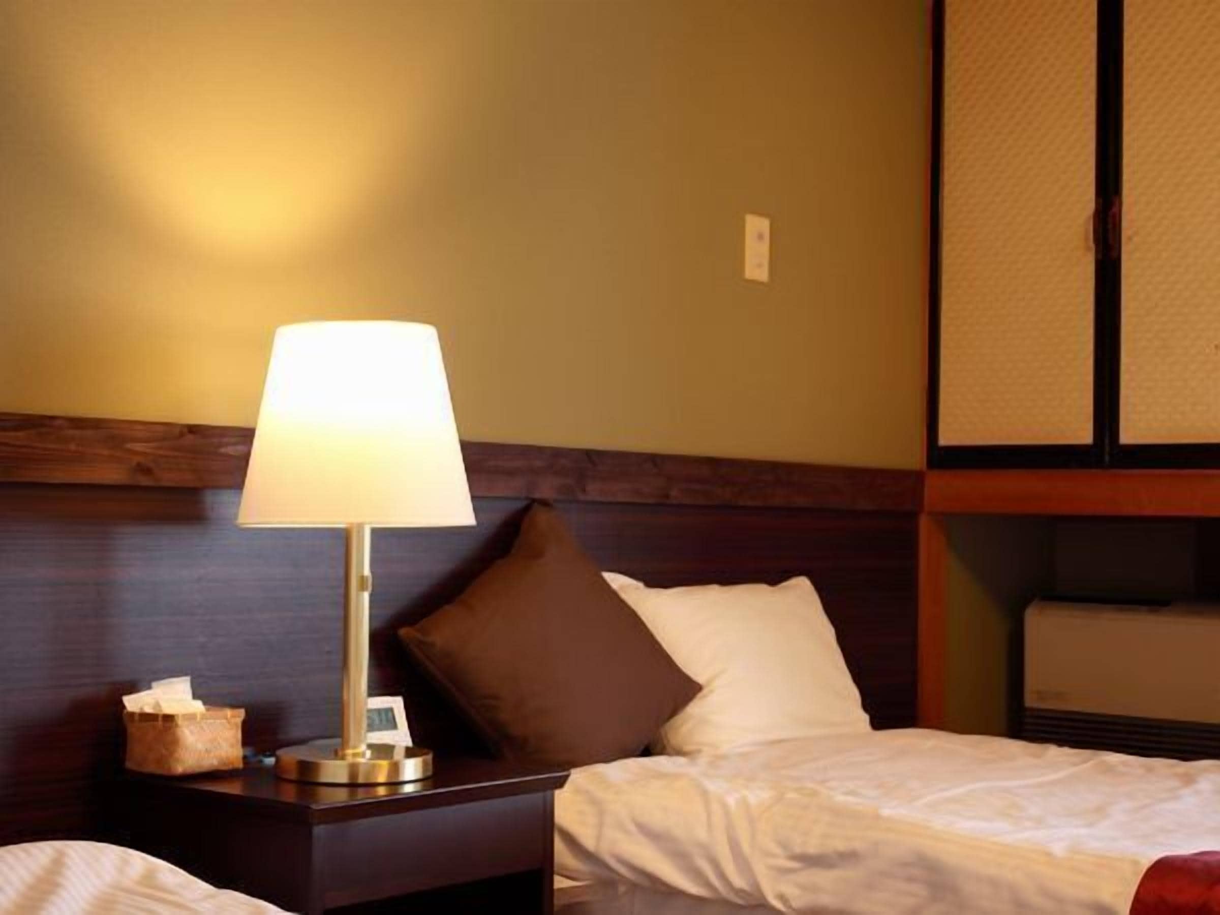 Una habitación de hotel con una cama, una mesita de noche con lámpara y un cabecero de madera.