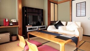 A modern living room with a flat-screen TV, a white sofa, a wooden coffee table, and a tatami mat floor. - Yakushikan (Komoro)