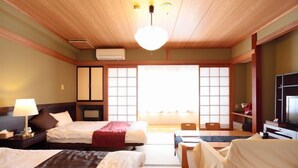 A hotel room with two beds, a desk, a chair, a television, and a large window with traditional sliding doors. - Yakushikan (Komoro)