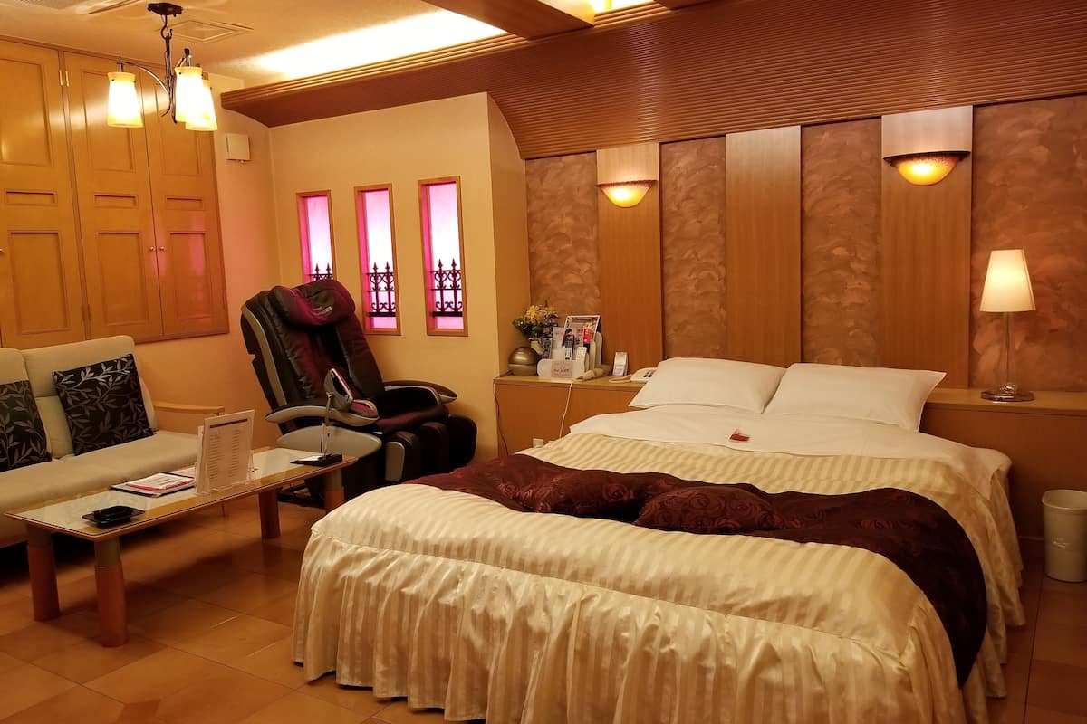 Ein Hotelzimmer mit einem Bett, einer Couch, einem Massagesessel, einem kleinen Tisch und einem Nachttisch mit Lampe.