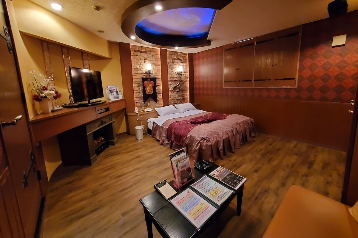 Ein Hotelzimmer mit Fernseher, Schreibtisch mit Computer, Bett mit Kopfteil, kleinem Tisch mit Speisekarte und Wandkleiderschrank.