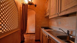 A narrow kitchen with wooden cabinets, a stainless steel sink, and a tiled floor. - Cala del Faro 103 (Arzachena)
