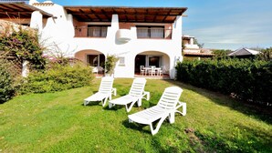 A two-story house with a patio area featuring three white lounge chairs. - Cala del Faro 103 (Arzachena)