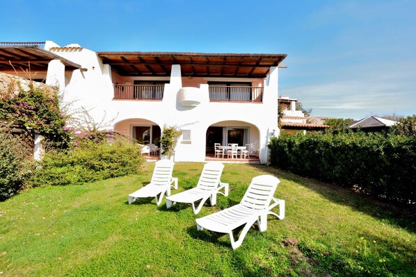 A two-story house with a patio area featuring three white lounge chairs.