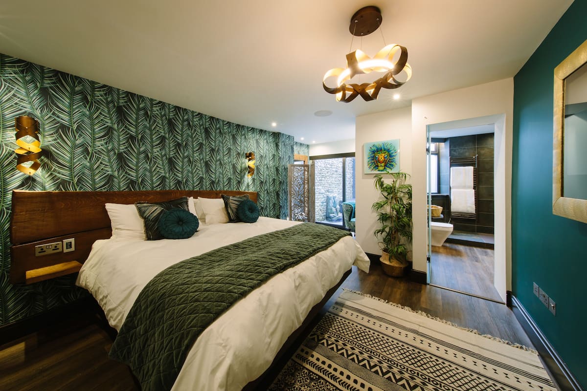 A modern bedroom with a large bed, a patterned wall, and a view of the bathroom.