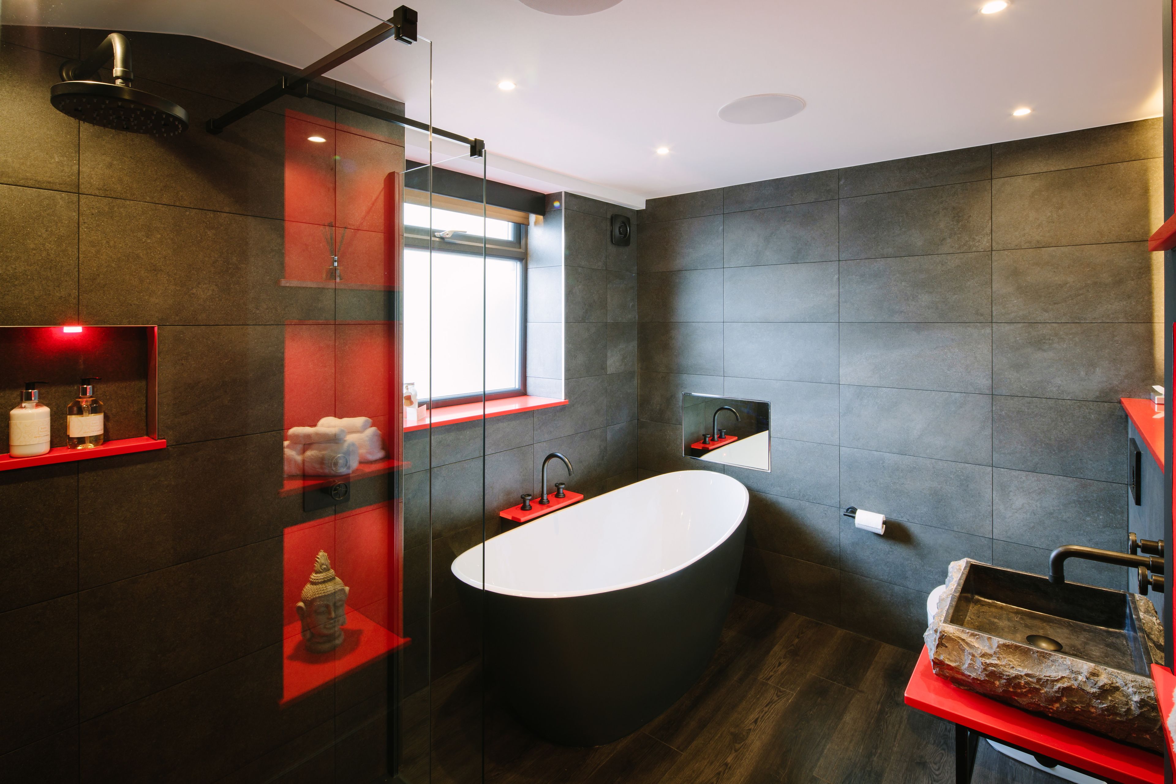 A modern bathroom with a freestanding bathtub, a glass-enclosed shower, and a red vanity with a sink.