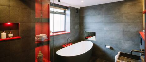 A modern bathroom with a freestanding bathtub, a glass-enclosed shower, and a red vanity with a sink.