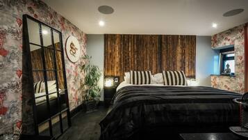 A modern bedroom with a large bed, a mirror, a wall-mounted TV, and a decorative plant.