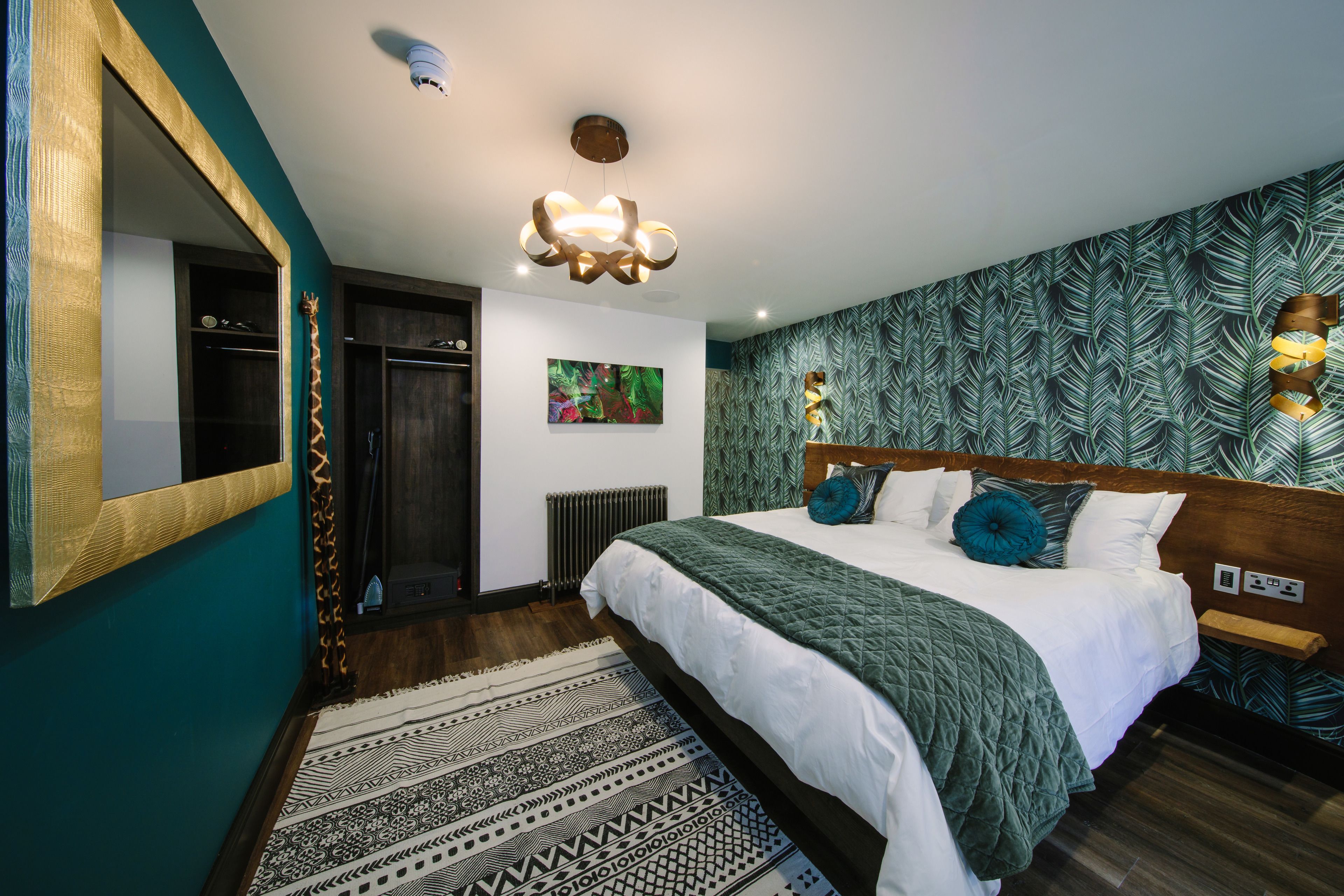 Een moderne slaapkamer met een groot bed, een spiegel, een plafondlamp en behang met een patroon.