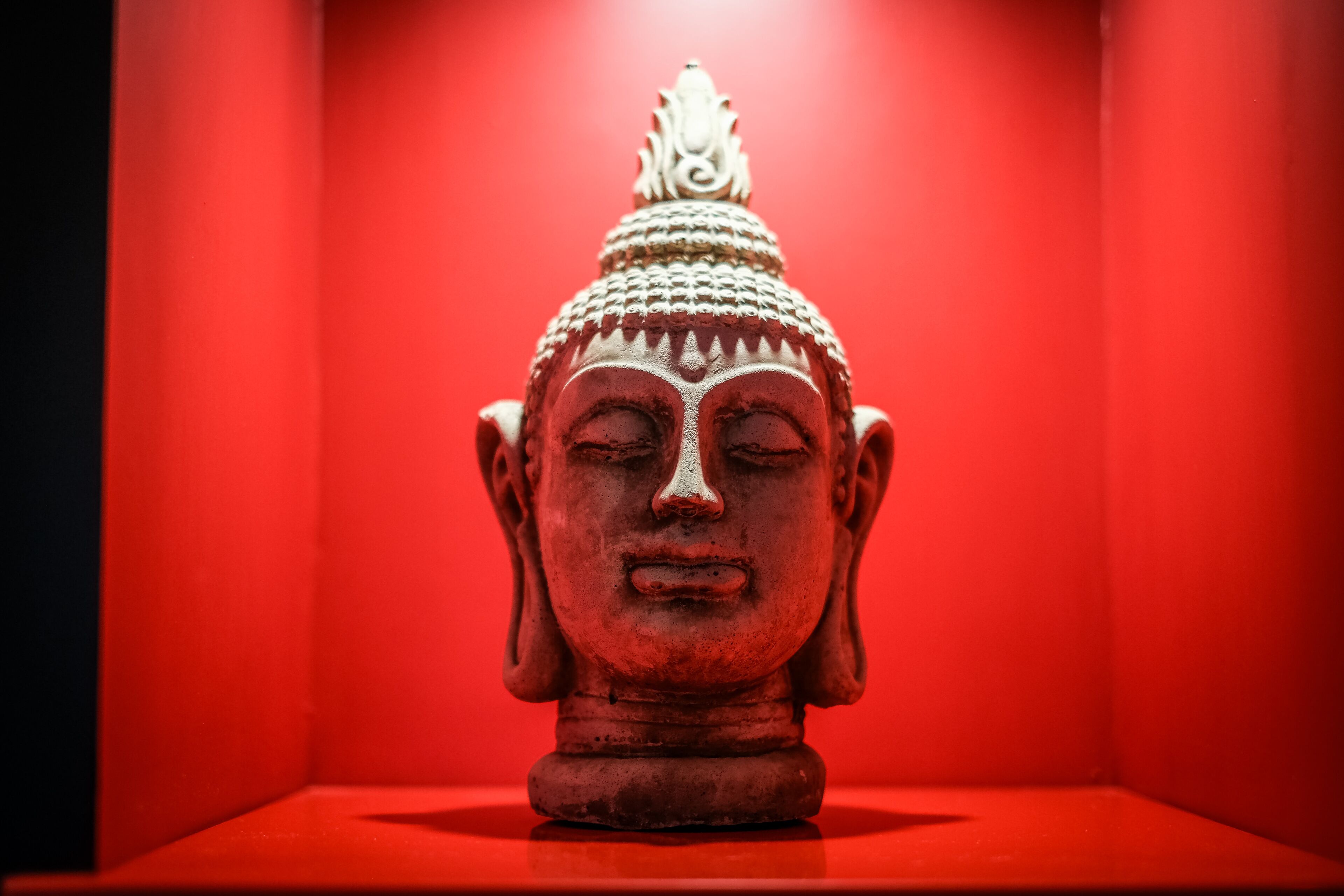 A statue with a detailed top and a base, set against a red background.