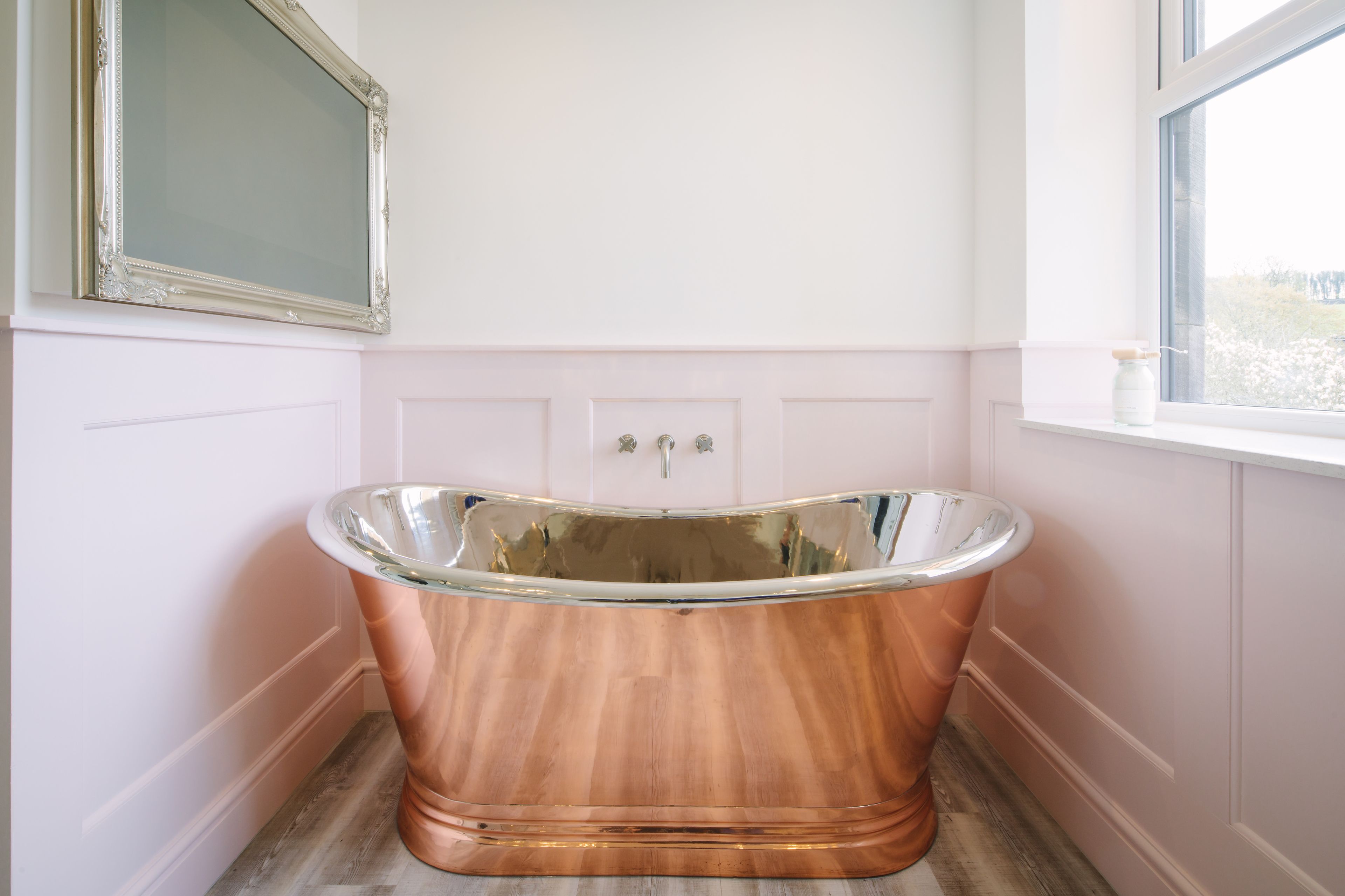 Un baño con una bañera de cobre, un espejo grande y una ventana con vistas.