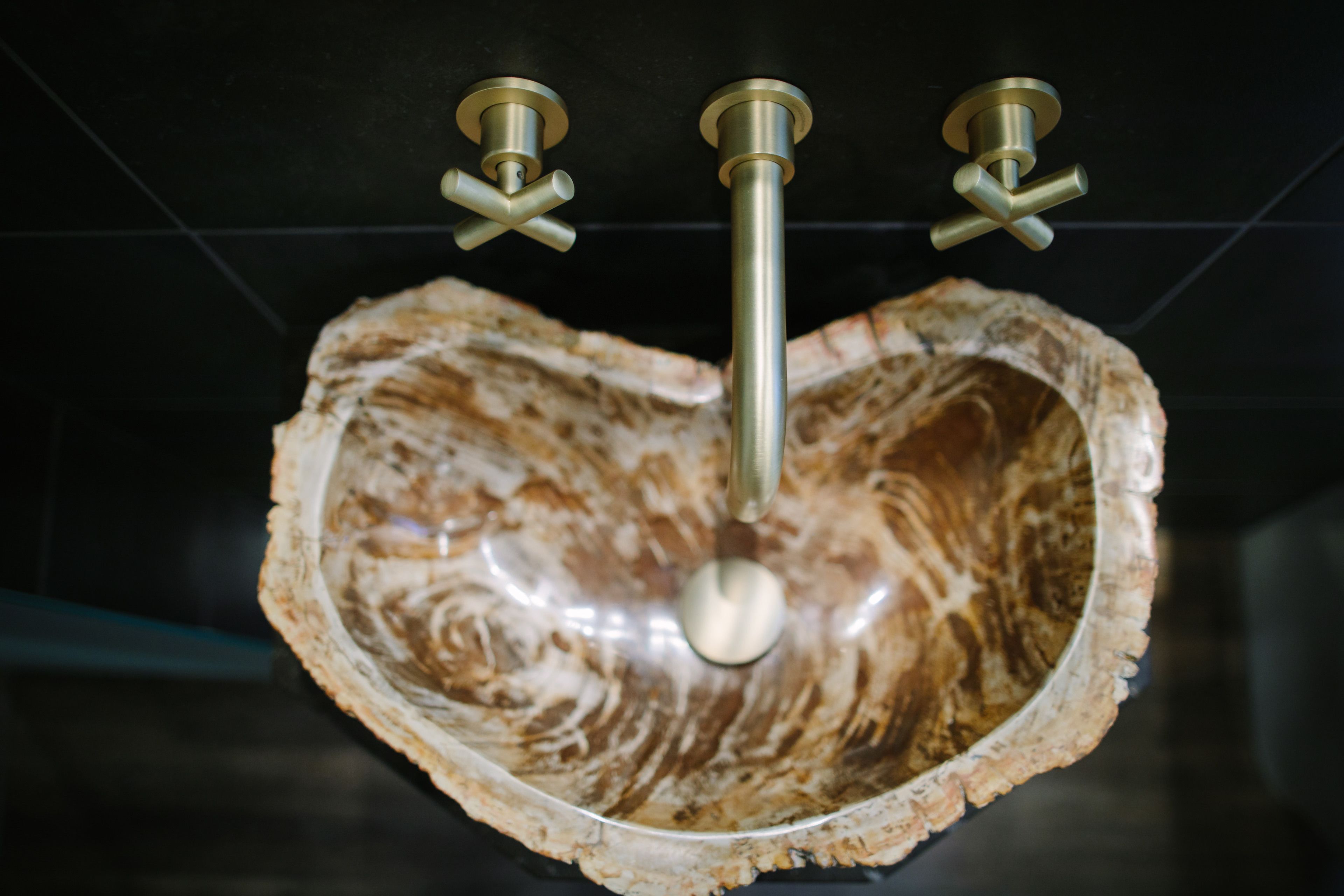 A heart-shaped sink with a central drain, mounted on a dark tiled wall.