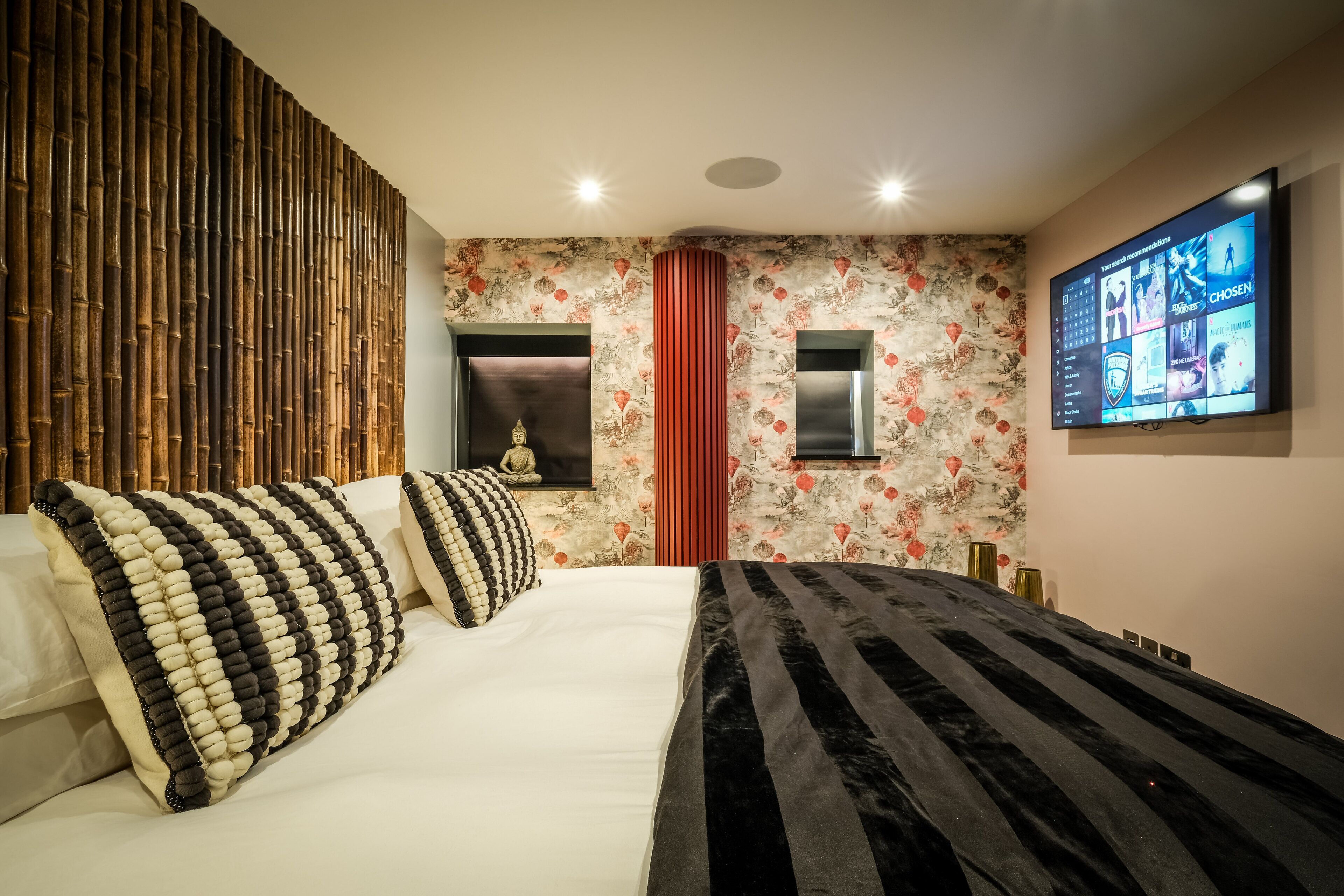 Un dormitorio moderno con una cama grande, un televisor montado en la pared y un panel decorativo.