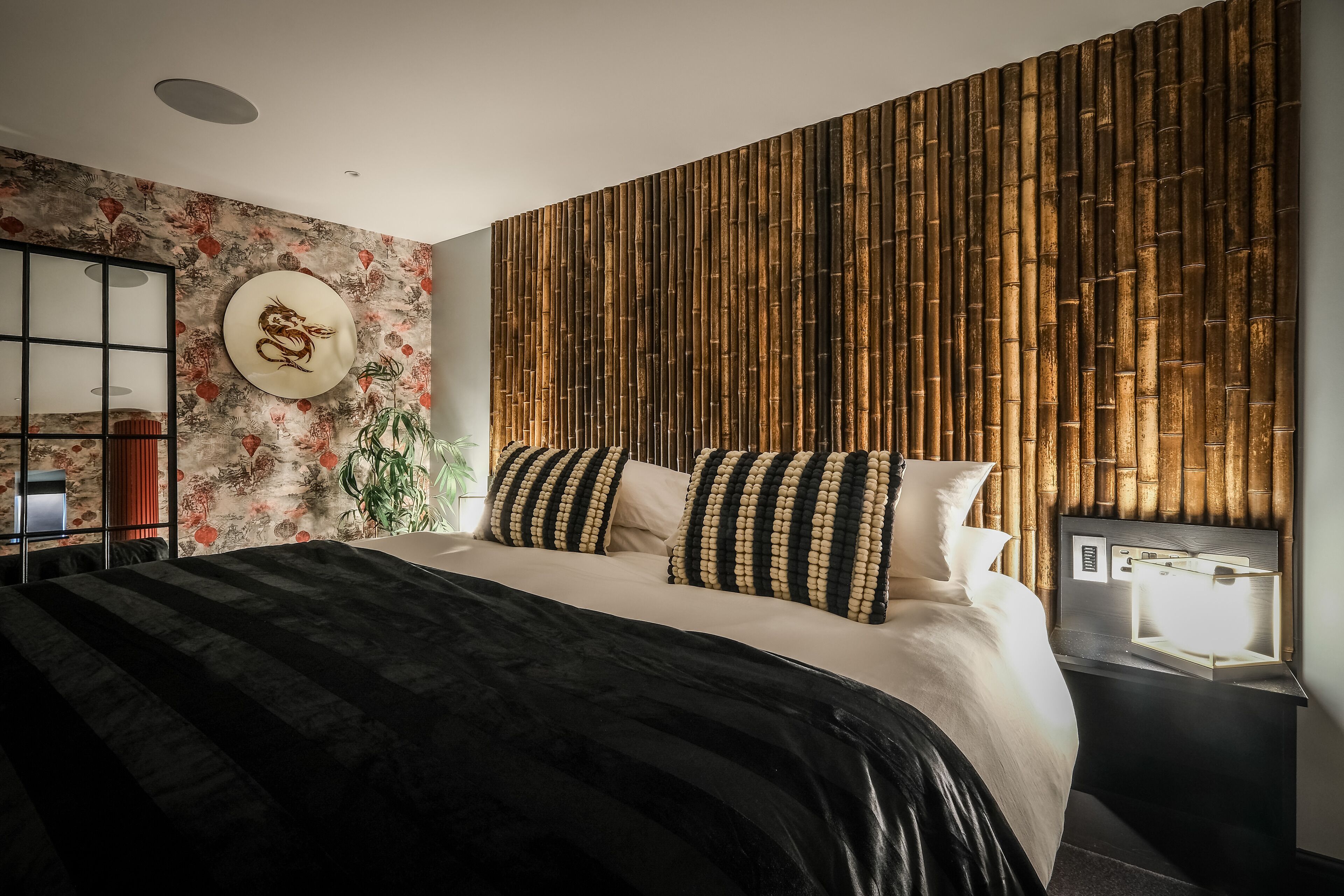 A modern bedroom with a large bed, a decorative wall panel, and a bedside table with a lamp.