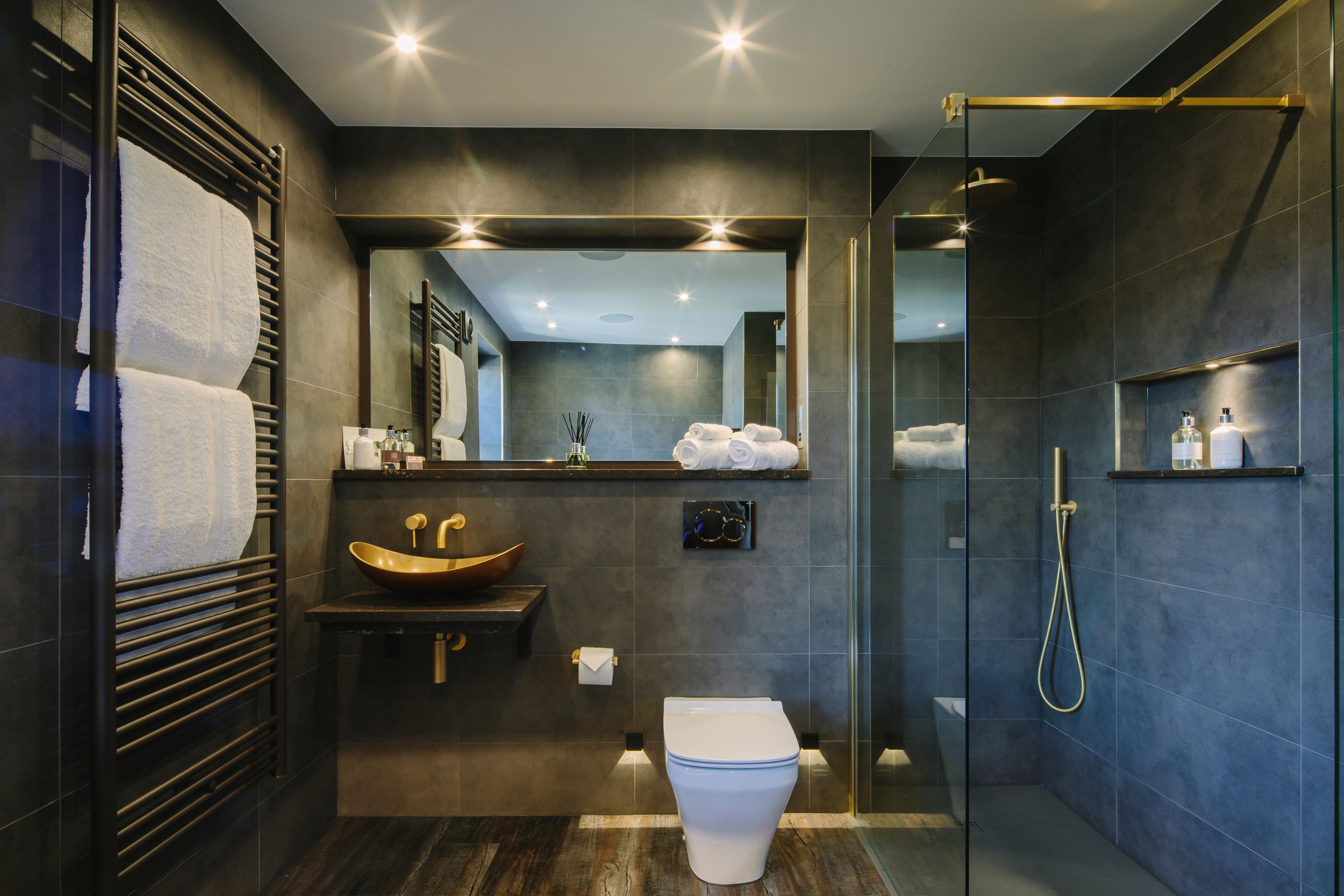 A modern bathroom with a large mirror, a vessel sink, a toilet, and a walk-in shower.
