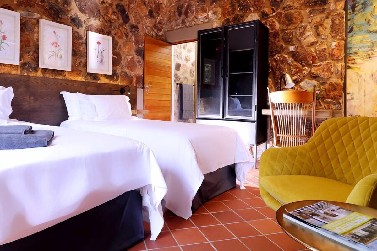 Ein Hotelzimmer mit zwei Betten, einer Steinsäule, einer Holztür und einem gelben Sessel.
