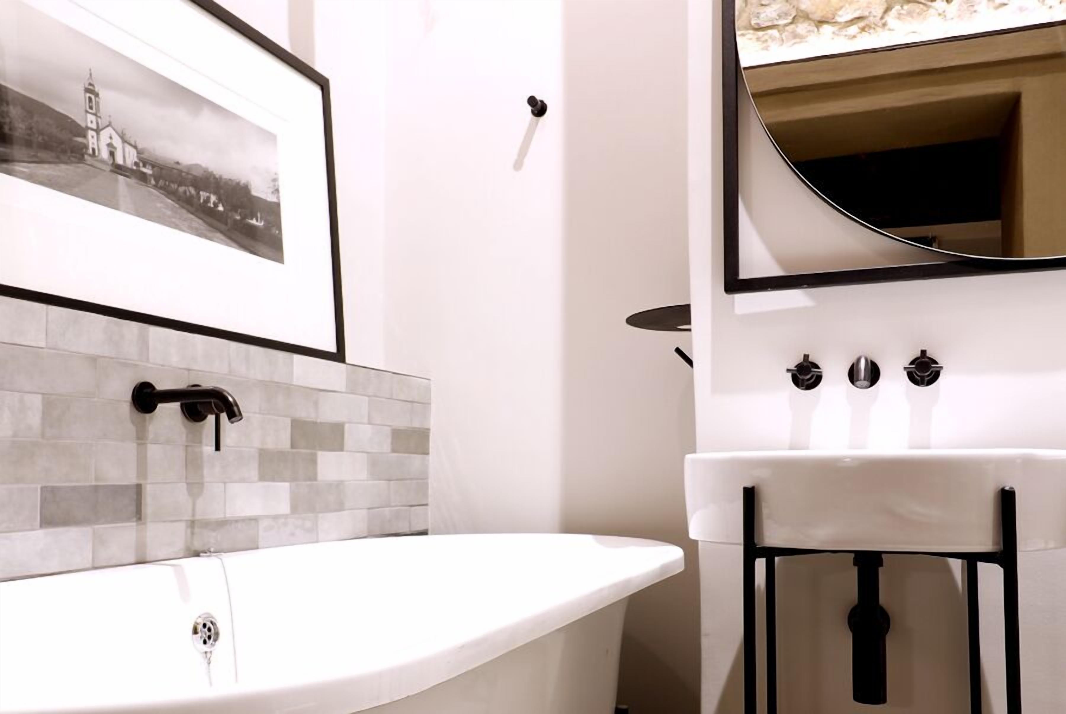 A modern bathroom with a freestanding bathtub, a white sink, and a framed photograph on the wall.
