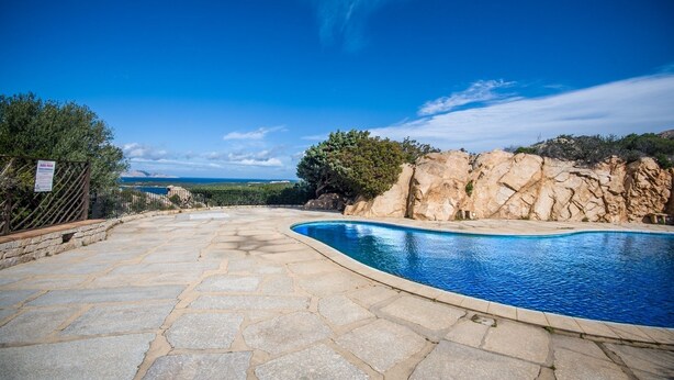 A stone pool with a clear blue sky and distant mountains. - Bloom 37 (Arzachena)