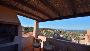 A balcony with wicker chairs and a grill, overlooking a scenic landscape. - Bloom 37 (Arzachena)
