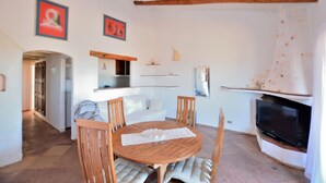 A dining area with a round wooden table and chairs, a white sofa, and a television mounted on the wall. - Bloom 37 (Arzachena)