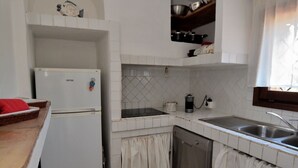 Cocina pequeña con gabinetes blancos, un refrigerador blanco, un lavamanos y un escurreplatos.