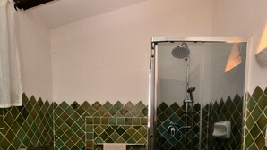 Baño con lavadora, inodoro y ducha con mampara de vidrio.