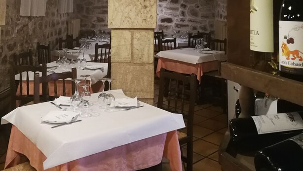 Un restaurante con paredes de piedra, vigas de madera y mesas dispuestas con copas de vino y cubiertos.