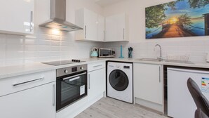 Une cuisine moderne avec des meubles blancs, un four à micro-ondes, une bouilloire, un lave-linge et un évier.