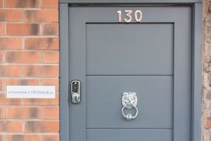 Een grijze deur met het nummer 130, een metalen deurklopper, en een bord waarop staat 'Townhouse @ 130 West St'.