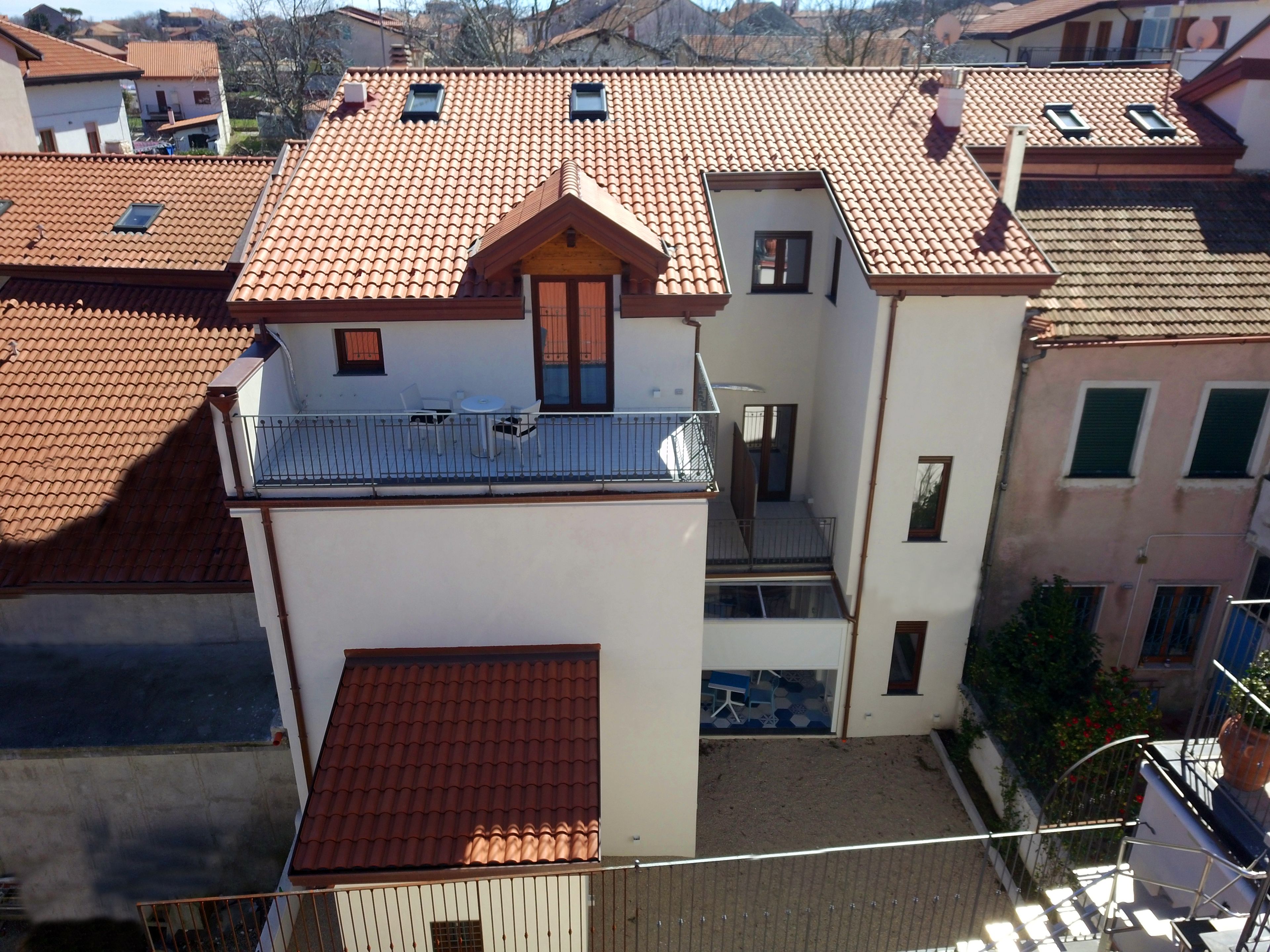 Un edificio a più piani con tetto in tegole rosse, balconi e un piccolo giardino.
