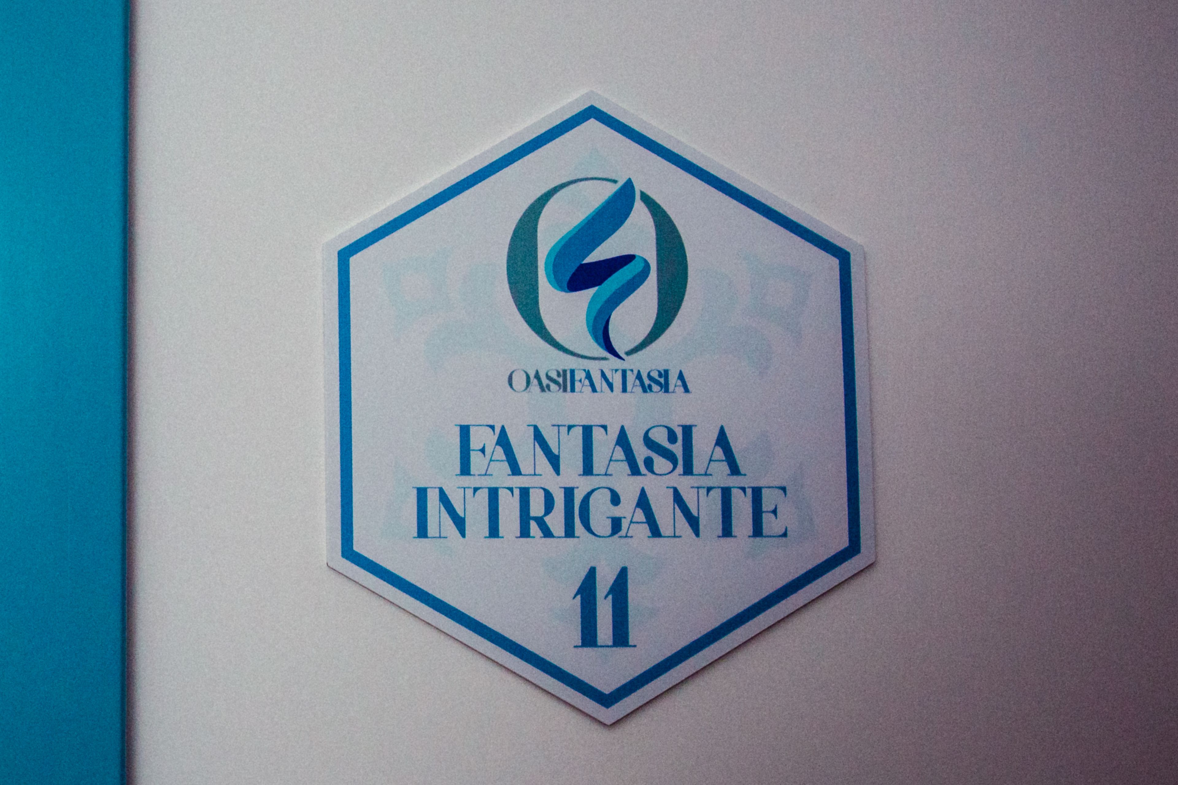 A hexagonal sign with a logo and text reading "OASIA FANTASIA INTRIGANTE 11".